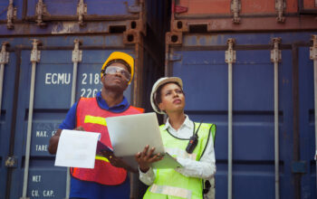 Worker man in hardhat and safety vest holding clipboard checklis Worker man in hardhat and safety vest holding clipboard checklist and Female foreman using laptop control loading containers box from cargo