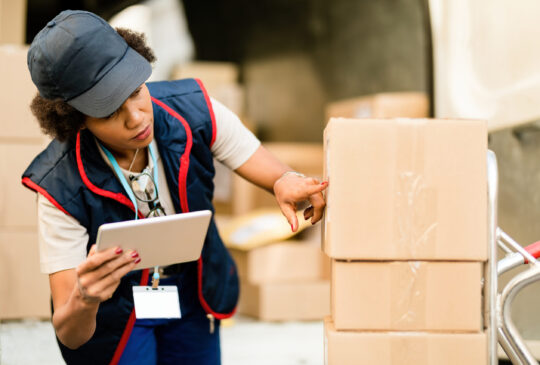 Black female courier getting reading for delivery and using digital tablet while checking address on a package.