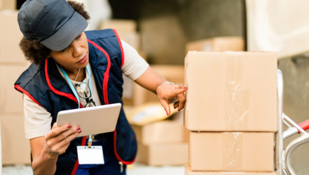 Black female courier getting reading for delivery and using digital tablet while checking address on a package.