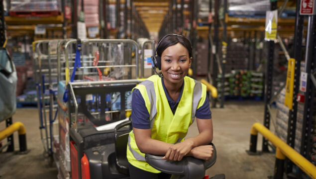 Woman leaning on a tow tractor in a distribution warehouse Woman leaning on a tow tractor in a distribution warehouse