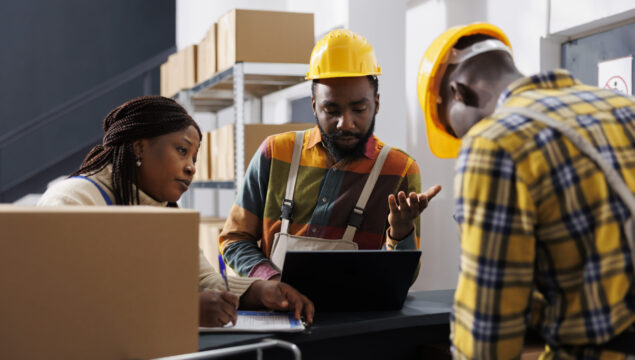 Logistics department managers planning stock supply schedule at counter Logistics department managers planning stock supply schedule at warehouse counter desk. All black storehouse employees team managing parcel registration and dispatching process