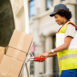 Happy black courier using hands truck while loading packages in a delivery van.