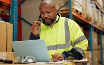 solution en courtage Man, phone call or laptop for logistics in warehouse, shipping or talking of order for distribution. Factory manager, smile or mobile for networking to import inventory or technology in manufacturing.